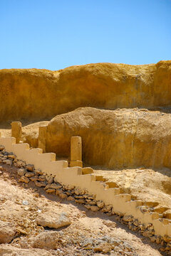 Stone stairs leading down along an arid coastal rock formation against a clear blue sky