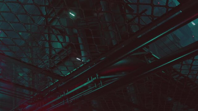 The scene shows an industrial structure at night, illuminated by blue and green lights. The view is taken from below a metal grid, creating a sense of depth and perspective.