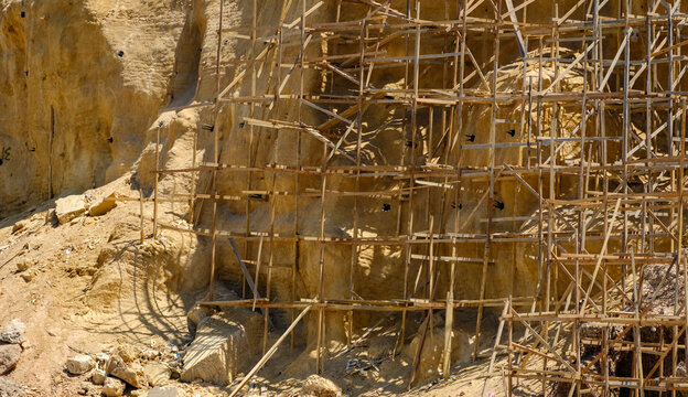 Wooden scaffolding structure built against a sandy mountain cliff for stabilization work