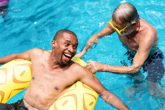 Two men enjoying a pool, one on a float, both smiling and relaxed.