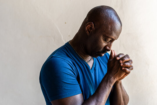 Man in blue shirt praying with hands clasped, looking thoughtful.