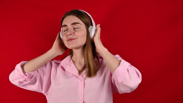  woman listens to music and dance in studio on red background. Headphones,sound and relax while listening to radio, streaming and joy. Valentine's day playlist