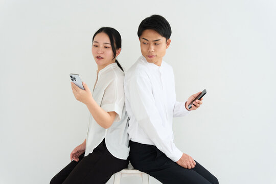 Young Japanese Man and Woman Back to Back Using Smartphones