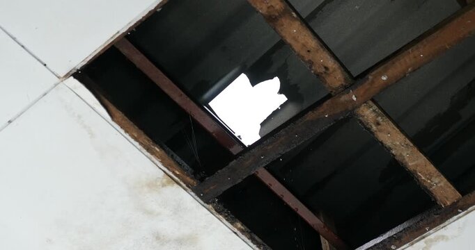 Damaged ceiling with hole exposing decayed wooden frame and broken roof