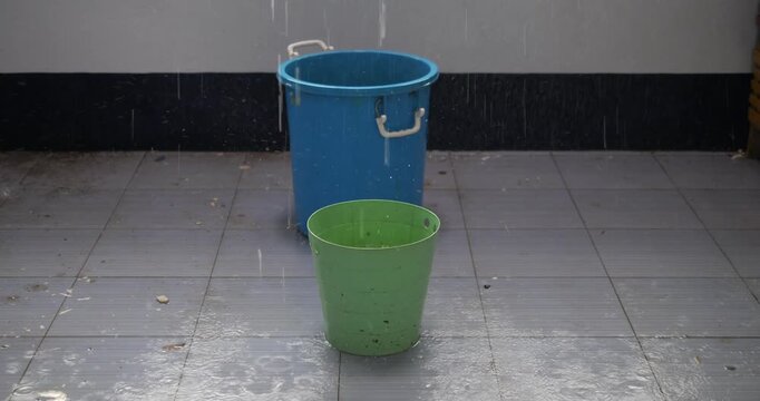Water leaking from ceiling into plastic buckets on floor during heavy rain