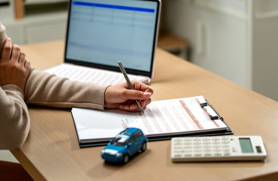 Woman filling out car loan application with pen on clipboard beside laptop and blue toy car