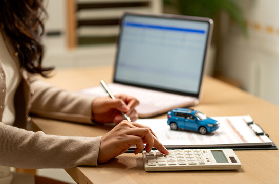 Woman calculating car loan with blue model vehicle on clipboard beside laptop