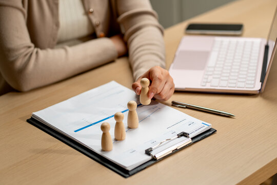 Hand placing wooden figures on financial chart with laptop and pen on wooden desk