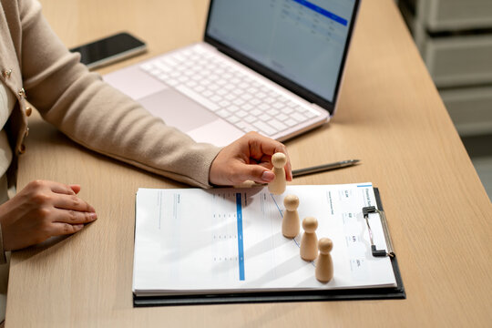 Hand placing wooden figurine on financial chart with laptop and pen on wooden desk