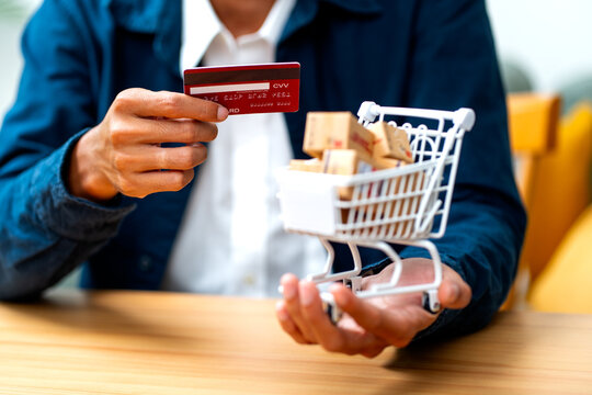 Person holding credit card and miniature shopping cart filled with parcel boxes