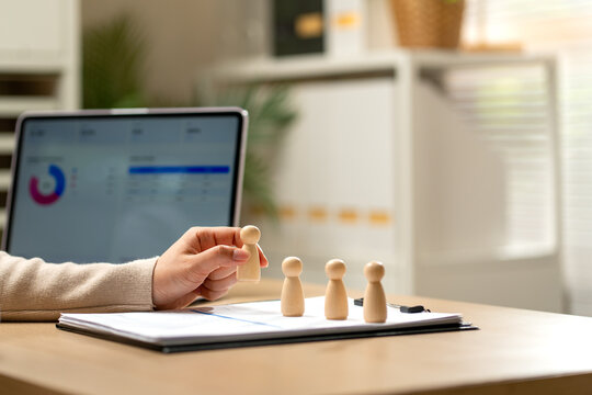Hand holding wooden figure over clipboard with financial charts on laptop in modern office