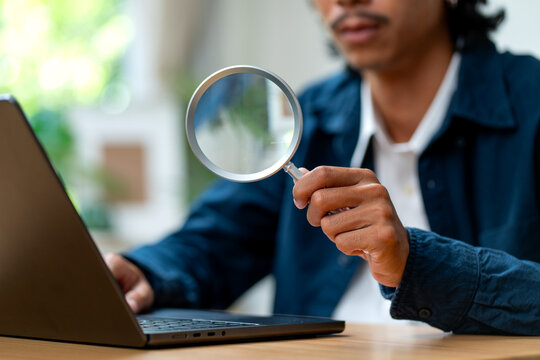 Hand holding magnifying glass over laptop screen in bright natural light