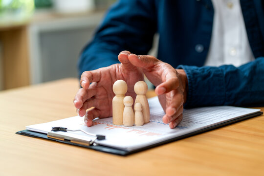 Hands gently cradling wooden family figures over financial documents on wooden desk