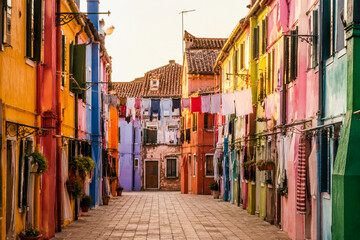 Fototapeta premium A narrow street with colorful houses and laundry lines in warm light.