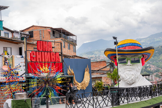 Comuna 13 street art featuring una chimba sign, colorful wind spinners, and a large statue with a colombian flag hat