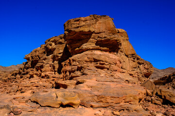 Massive weathered sandstone rock formation rising in a barren desert landscape under a clear blue sky © Buğra Kaan Ersoy
