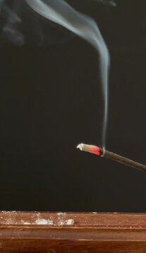 Lit aromatic incense stick releasing pleasantly scented smoke, in a wooden holder. Aromatherapy, meditation, relaxation, spirituality, and yoga concept, with a calming atmosphere.