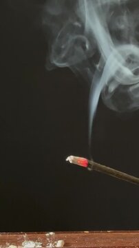 Lit aromatic incense stick releasing pleasantly scented smoke, in a wooden holder. Aromatherapy, meditation, relaxation, spirituality, and yoga concept, with a calming atmosphere.