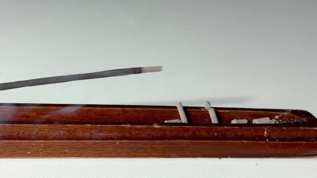 Lit aromatic incense stick releasing pleasantly scented smoke, in a wooden holder. Aromatherapy, meditation, relaxation, spirituality, and yoga concept, with a calming atmosphere.v