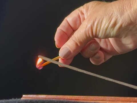 Lit aromatic incense stick releasing pleasantly scented smoke, in a wooden holder. Aromatherapy, meditation, relaxation, spirituality, and yoga concept, with a calming atmosphere.