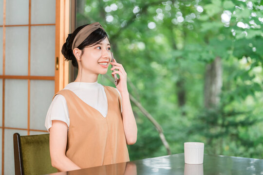 A Japanese woman talking on her smartphone in a room with a view of a newly recorded forest.