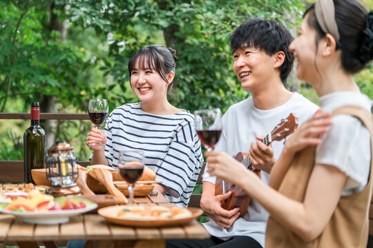 Young Asian men and women, friends, colleagues, and coworkers enjoying a barbecue, home party, and glamping on a wooden deck.