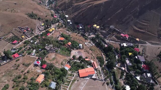 Drone view of North Road houses with red roofs dotted across a brown hillside, a mountain settlement above the valley floor. Ideal for travel, tourism, and nature stock Iran Alborz valleys.