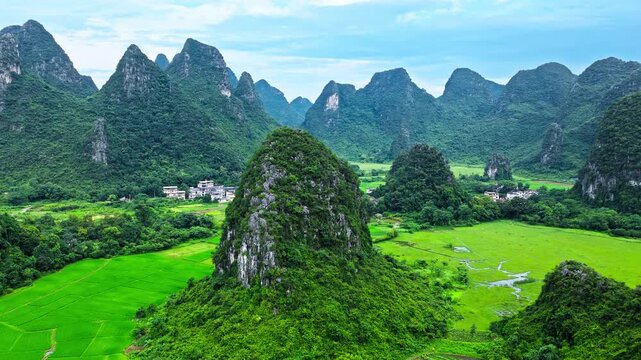 Aerial view of a lush green karst hill overlooking a vast agricultural valley with a village and fields in Guilin, China