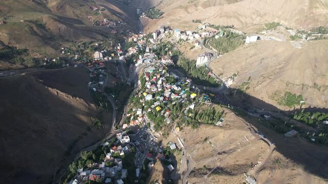 Shem village crowds a mountain fold in an aerial frame, rooftops stepping down the valley beside arid Iranian slopes. Ideal for travel, tourism, and nature stock Iran Alborz mountains.
