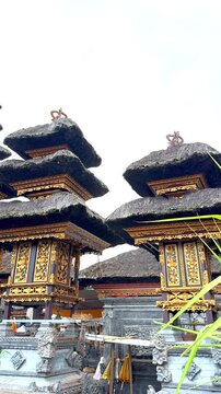 Low angle view of Balinese meru roofs with gilded carved pavilions, stacked thatch tiers, stone bases and foreground tropical plants in heritage temple setting, with temple, meru, roof, thatch detail