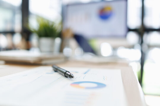 Pen rests on a financial report displaying a pie chart and graphs, representing business analysis, strategic planning, and market research on a blurred office desk