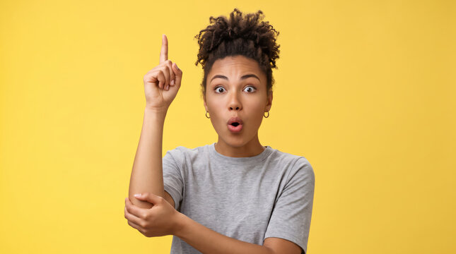 Surprised young woman pointing finger up in eureka moment.