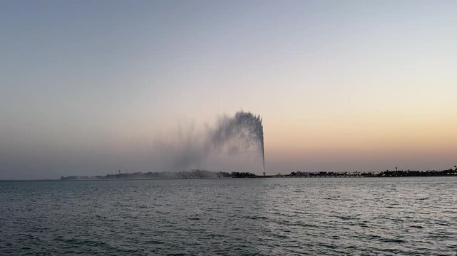 Wide static shot of King Fahd Fountain spraying water high into the sky over the Red Sea in Jeddah at dusk.