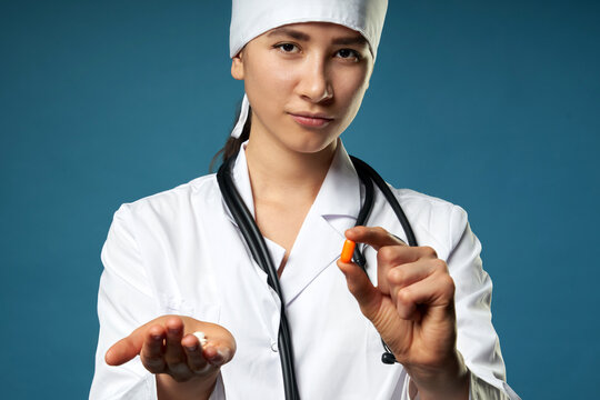 Young female doctor holding a pill, looking at it and giving it as a treatment to the patient
