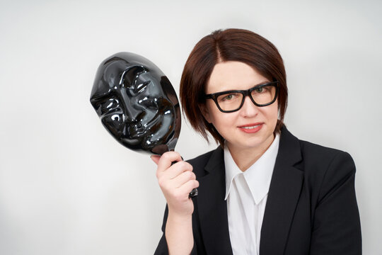 Young businesswoman wearing black formal suit standing and holding black plastic mask, hiding concept with copy space