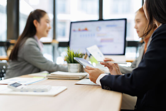 Businesswomen analyzing financial charts and reports on a computer screen and digital tablets during a collaborative meeting, focusing on corporate strategy and data driven decisions