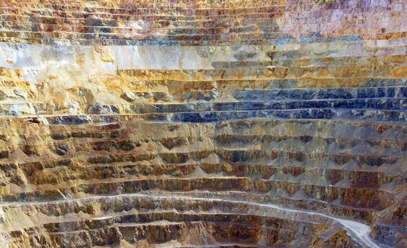 Steep, terraced benches of the Roșia Poieni copper mine, a massive open-pit excavation located in the Apuseni Mountains of Alba County, Romania.