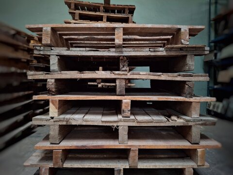 Close up of a tall stack of empty wooden pallets in an industrial warehouse. Essential equipment for logistics, supply chain, and inventory management. Shipping and freight storage concept.
