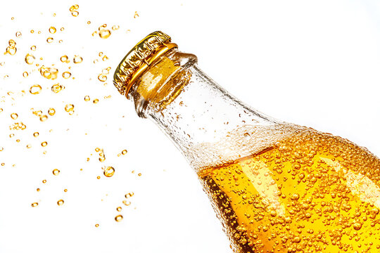 Refreshing golden beverage with bubbles exploding from an open glass bottle.