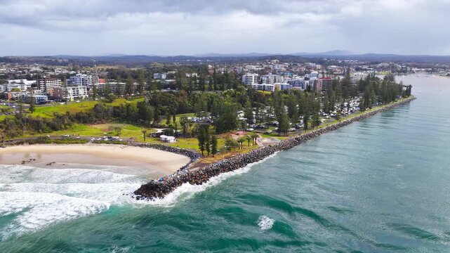 Aerial video tracking along the Port Macquarie breakwall, showing Town Beach, the nearby caravan park, Hastings River entrance and surrounding coastal landscape in New South Wales, Australia.