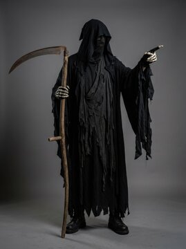 Grim reaper figure in black tattered hooded robe holding wooden scythe and pointing skeletal hand against gray studio background.