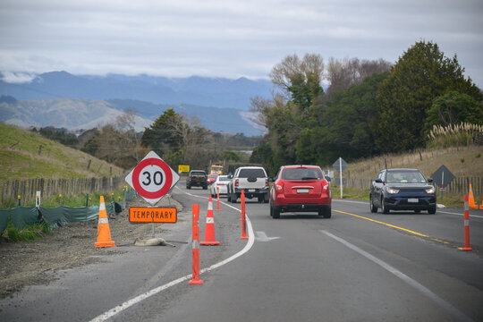 Temporary 30 km/h road sign and traffic cones by the side of road. Cars and trucks driving slowly on the road. Roadworks in North Island.