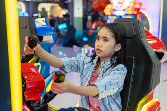 Young Asian girl with an intense, focused expression playing an arcade simulator game. Family entertainment, recreation concept.