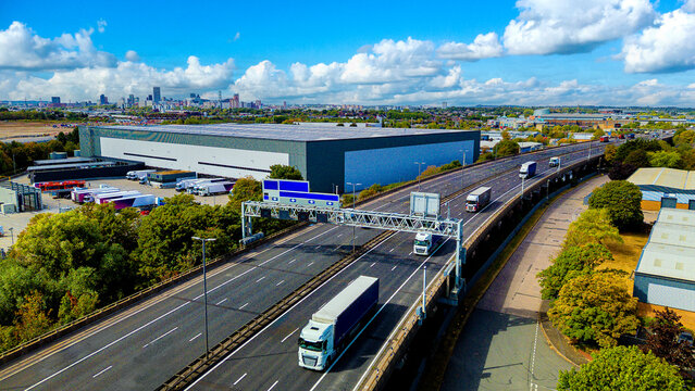 Freight trucks moving along elevated motorway near large distribution warehouse