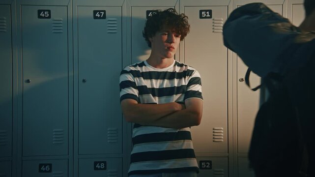 Concerned High School Boy Wearing Striped T Shirt, Stands Silently Against Metal Lockers During School Break While Students Pass Nearby. Concept of Academic Stress, Low Grades and Emotional Tension.