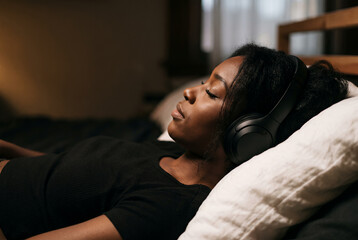Fototapeta premium Woman resting on bed with headphones in peaceful home setting