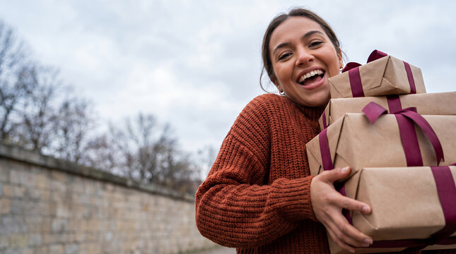 Young woman holding wrapped gift boxes in her arms outdoors on winter day