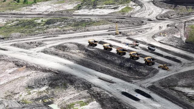 An aerial view of rigid dump trucks and excavators parked in a row at a coal mine