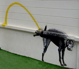 Black dog mural with yellow leash graffiti on a white wall. © sen
