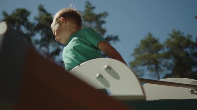 Happy smiling young boy at the top of a wooden playground. Portrait of a joyful kid playing outdoors at a neighborhood playground. Happy kid enjoying activities at a park.